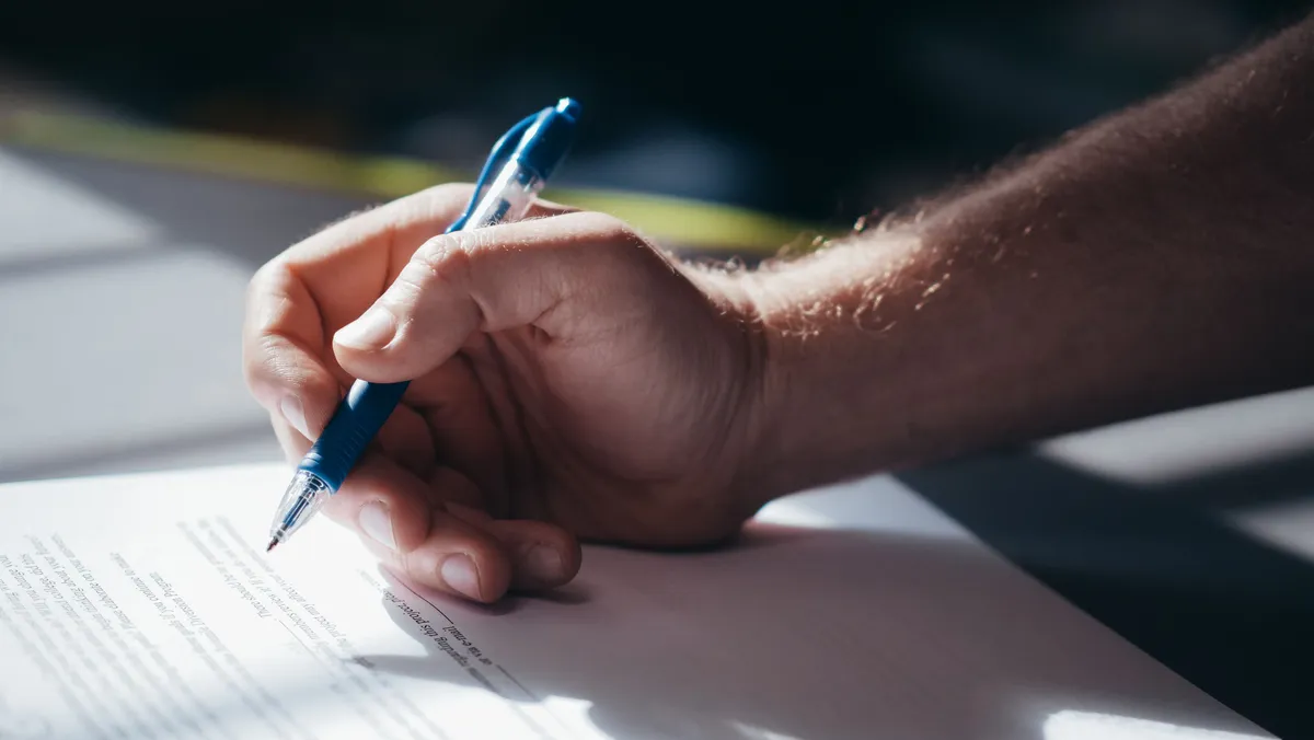 Mão assinando um documento com caneta azul