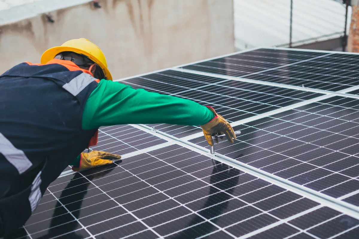 Técnico de capacete instalando painéis solares num telhado
